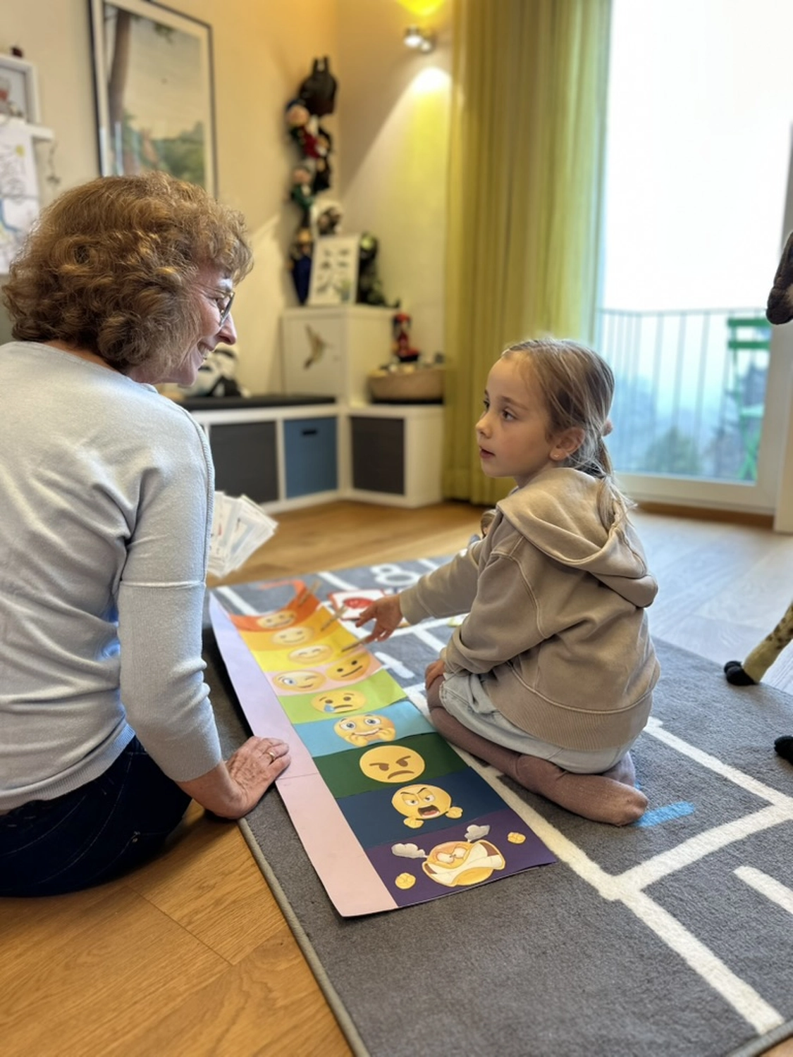 Zeit & Raum für Sie und Ihr Kind – Erzieherin und Heilpädagogin – Dieses Bild zeigt eine Frau und ein Mädchen, die an einem kleinen Tisch in einem Raum sitzen, möglicherweise für eine Lernsitzung oder Aktivität. Der Raum ist mit verschiedenen Gegenständen dekoriert, darunter einem Buch mit dem Titel „Sarah schafft das“.